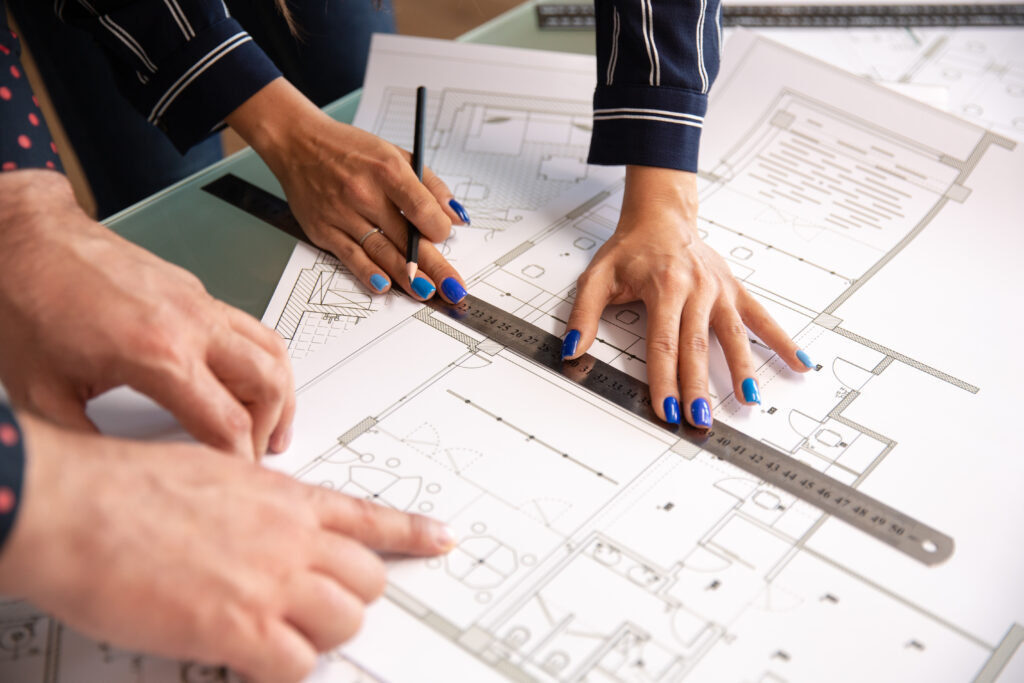 Close up of two architects' hands checking a house plan with a ruler and pencil, focusing on precise integration of electronic locking systems.