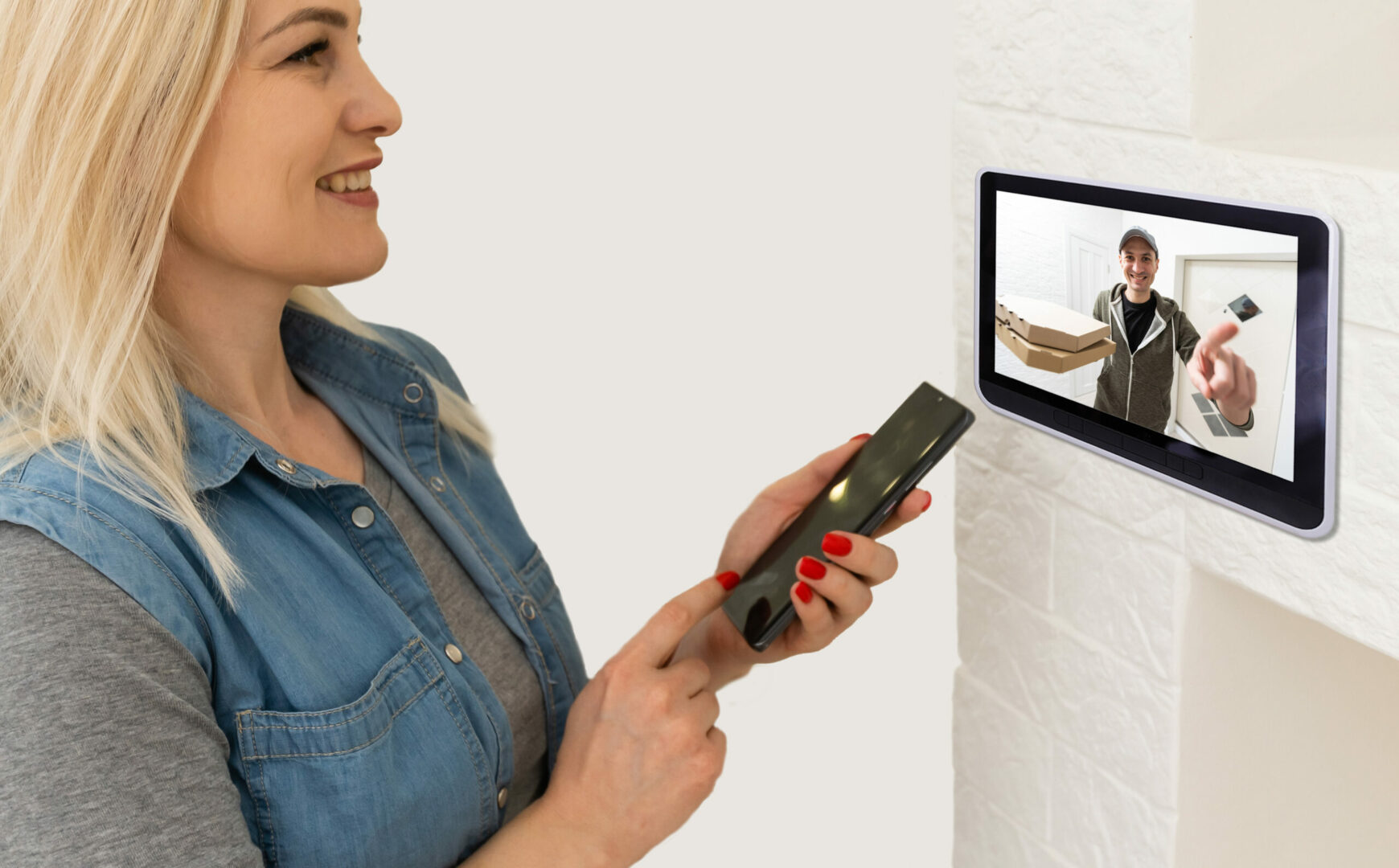 Woman monitoring a delivery man on a security camera through a tablet, highlighting the use of commercial intercom systems for enhanced security and communication.